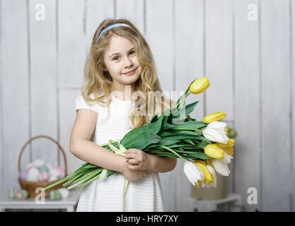 Portrait of cheerful little blonde girl with tulips bouquet on white wood background. Stock Photo