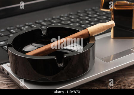 Close-up cigar in the ashtray standing on a laptop. Habits person Stock Photo