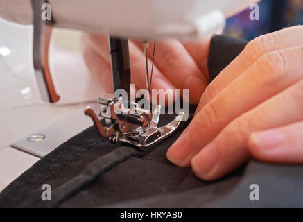 Hands seamstress crosslinking dark dense tissue on a modern sewing machine Stock Photo
