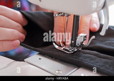 Hands seamstress crosslinking dark dense tissue on a modern sewing machine Stock Photo