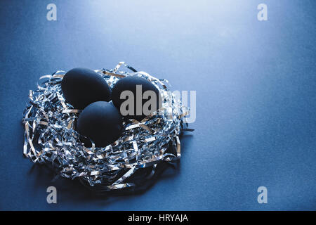 Three black eggs in a nest made of silver strings, on a dark blue background, Easter concept Stock Photo