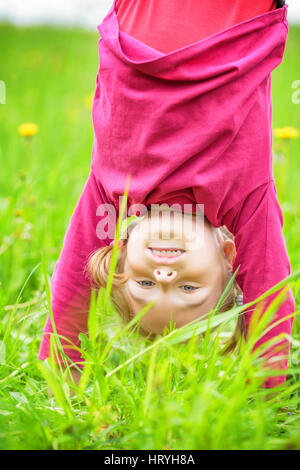 Happy little girl standing upside down on grass in summer park Stock Photo