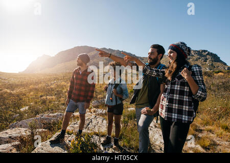 Group of friends on hike pointing away at a view. Young people hiking on extreme terrain on a summer day. Stock Photo