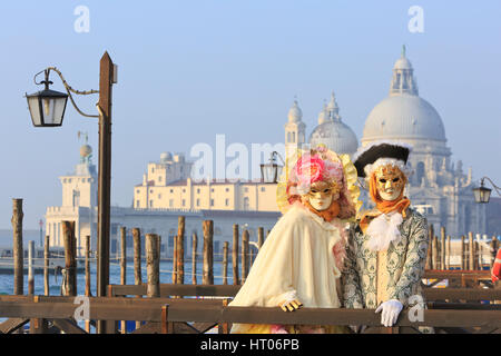 A couple in traditional Venetian masks outside the Santa Maria della Salute Basilica Church during the Carnival in Venice, Italy Stock Photo