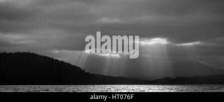 Rays of sunlight penetrating dark clouds over Loch Garry and dense conifer woods, Lochaber, Scotland, September 2016. Stock Photo