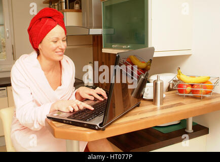 Junge Frau im Morgenmantel arbeitet am Notebook in der Kueche - woman in bath robe using laptop in kitchen Stock Photo