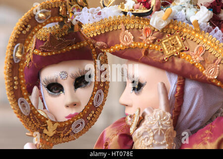 A masked lady looking at herself in a mirror outside the Doge's Palace during the Carnival of Venice, Italy Stock Photo