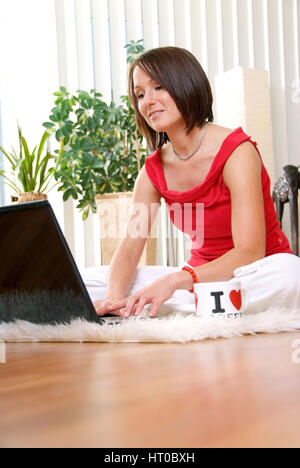 Junge Frau mit Laptop sitzt gem?tlich auf Teppich am Wohnzimmerfu?boden - young woman at home using laptop Stock Photo