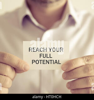 Closeup on businessman holding a card with text REACH YOUR FULL POTENTIAL, business concept image with soft focus background and vintage tone Stock Photo