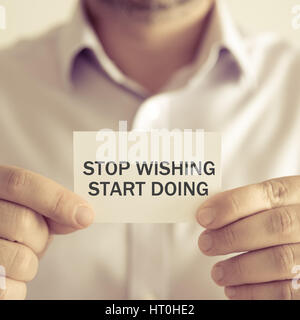 Closeup on businessman holding a card with text STOP WISHING START DOING, business concept image with soft focus background and vintage tone Stock Photo