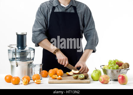 Anonymous man wearing an apron, preparing healthy freshly made fruit juice, using modern electric juicer, healthy lifestyle concept on white backgroun Stock Photo