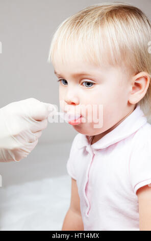 Close-up shot of pediatrician giving a dose spoon of cough syrup to little patient Stock Photo