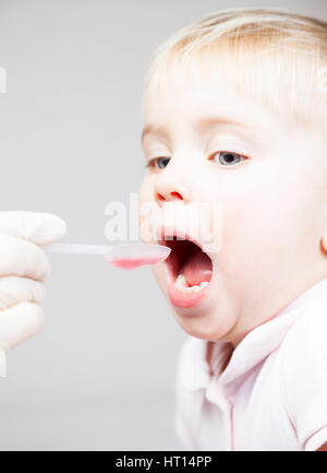 Close-up shot of pediatrician giving a dose spoon of cough syrup to little patient Stock Photo