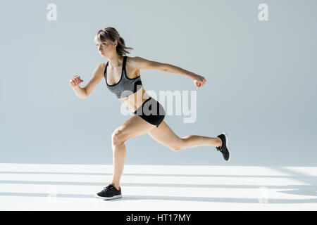 side view of running woman in sportive clothing on grey Stock Photo
