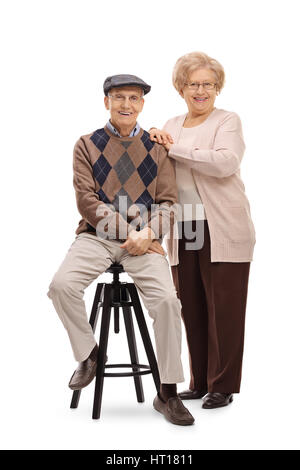 Full length portrait of an elderly man sitting on a chair with an elderly woman standing next to him isolated on white background Stock Photo
