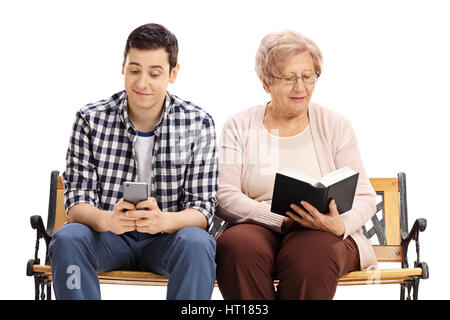 Young man using a phone and sitting on a bench with a mature woman reading a book isolated on white background Stock Photo