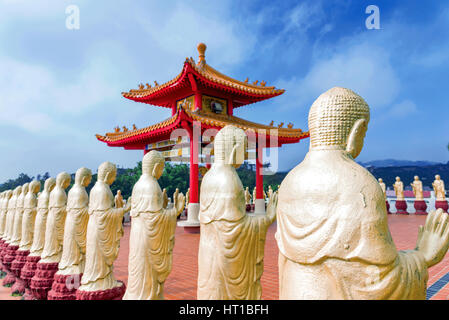 Row of golden Buddha statues with blurred temple in the background Stock Photo