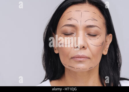 Not perfect. Serious dreamy young mature lady posing for a photographer with lines drawn upon her face and standing isolated on white background Stock Photo