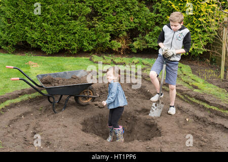 young girl and boy digging wildlife pond in garden Stock Photo