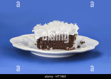 A piece of chocolate cake with fluffy white frosting topped with shreded coconut on a white serving bplate. Oklahoma, USA. Stock Photo