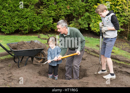 grandfather father with children digging wildlife pond in garden Stock Photo