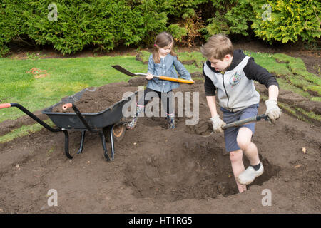 young girl and boy digging wildlife pond in garden Stock Photo