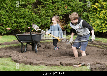 young girl and boy digging wildlife pond in garden Stock Photo