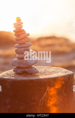 Tower of pebbles with shell on top at bright evening sunshine, built on wooden groin Stock Photo