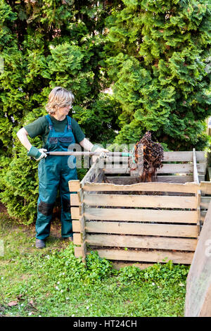 Young caucasian female tumbling the compost with a pitch fork Stock Photo