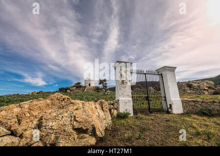 Wispy clouds above large iron gates and painted stone pillars leading to the steps to a large white domed mausoleum at Palasca in the Balagne region o Stock Photo