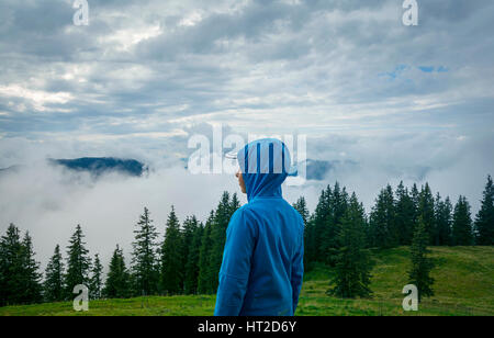Young boy standing on the peak and looking to the misty landscape, in the Kitzbuhel mountains, Tirol, Austria Stock Photo