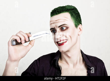 guy with crazy joker face holding knife, green hair and idiotic smike. carnaval costume. Stock Photo