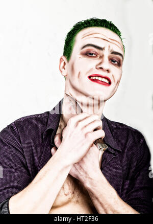 guy with crazy joker face holding knife, green hair and idiotic smike. carnaval costume. Stock Photo