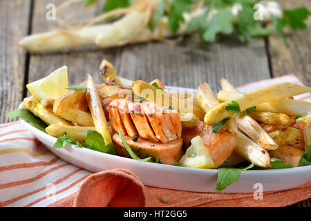 Roasted  white asparagus with fried salmon served on rocket salad leaves in a white bowl Stock Photo