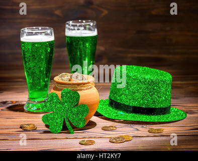 St Patricks day with glasses of green beer, leaf clover, leprechaun hat and pot full gold coins on vintage wooden background, close up Stock Photo