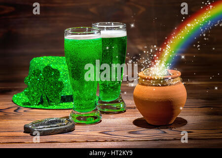 St Patricks day with glasses of green beer, shamrock, leprechaun hat, horseshoe, pot full gold coins and rainbow on vintage wooden background, close u Stock Photo