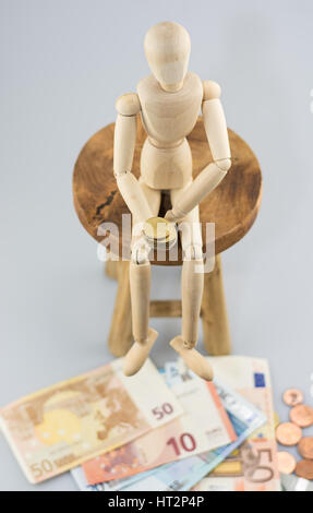 Mannequin sitting on a chair and holding a coin. Stock Photo