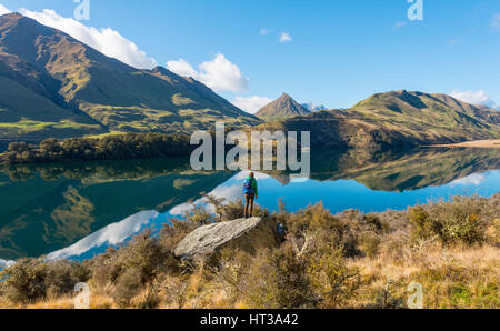 Hiker standing on rocks, mountains reflecting in lake, Moke Lake near Queenstown, Otago Region, Southland, New Zealand Stock Photo