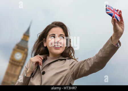 Girl or young woman tourist on vacation taking a selfie photograph by Big Ben with Union Jack cell phone, London, England, Great Britain Stock Photo