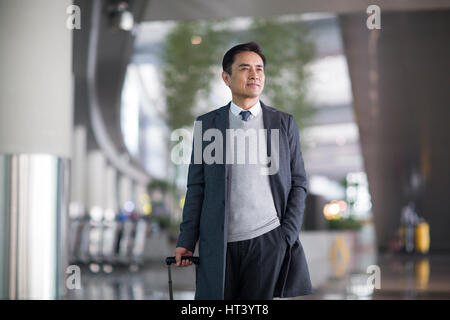 Businessman with wheeled luggage in airport lobby Stock Photo