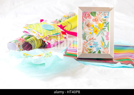 Decorative paper, small pieces of colorful fabric and a frame filled with a floral pattern on top of a white sheet Stock Photo