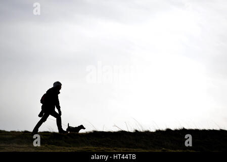 Silhouette of a woman walking a dog on a cloudy day Stock Photo