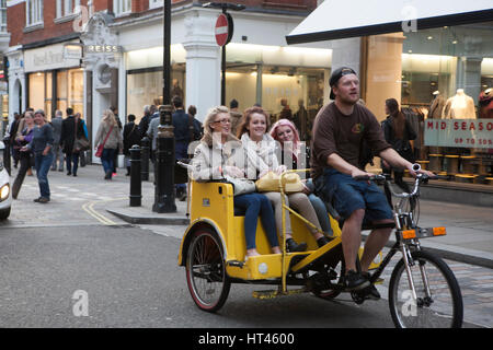 LONDON, UK - 16TH MARCH 2016: A man riding a Rickshaw with happy women in the back down a street in London Stock Photo