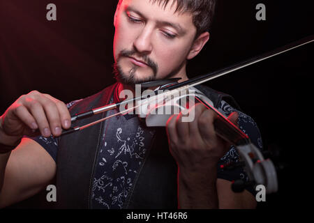 Young bearded man playing a white electric violin, isolated on a black background Stock Photo