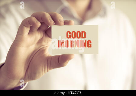 Closeup on businessman holding a card with text GOOD MORNING, business concept image with soft focus background and vintage tone Stock Photo