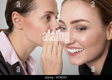 Close up shot of two happy, pretty business women, sharing a secret and whispering in each others ear. Stock Photo
