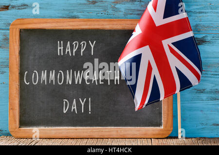 a wooden-framed chalkboard with the text happy commonwealth day written in it and the Union Flag against a blue rustic wooden background Stock Photo