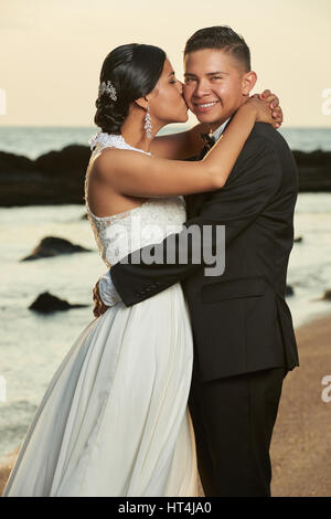 Portrait of hispanic wedding couple. Happy bride and groom kissing on ocean sunset beach Stock Photo