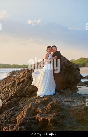 Hugging bride and groom standing on rock at sunny sunset time with copy space. Stock Photo