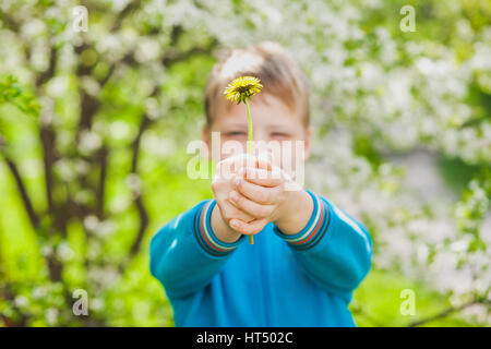 Closeup portrait of cute funny little boy isolated over green blooming trees background. Caucasian blonde child enjoying sunny warm weather in spring  Stock Photo